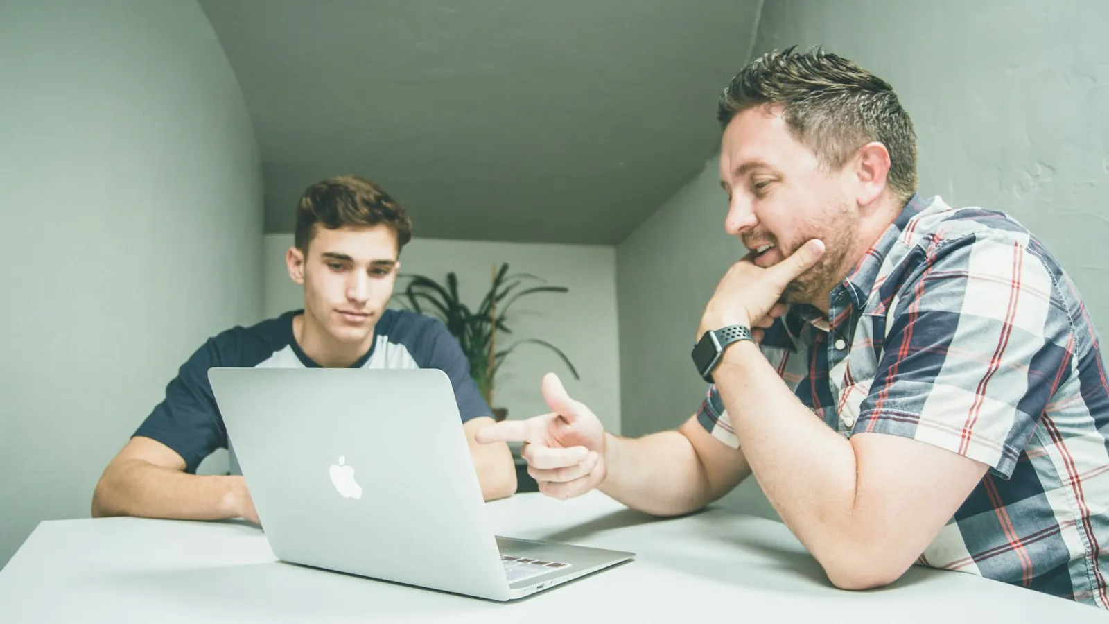 En eldre mentor forklarer noe til en yngre person ved en laptop